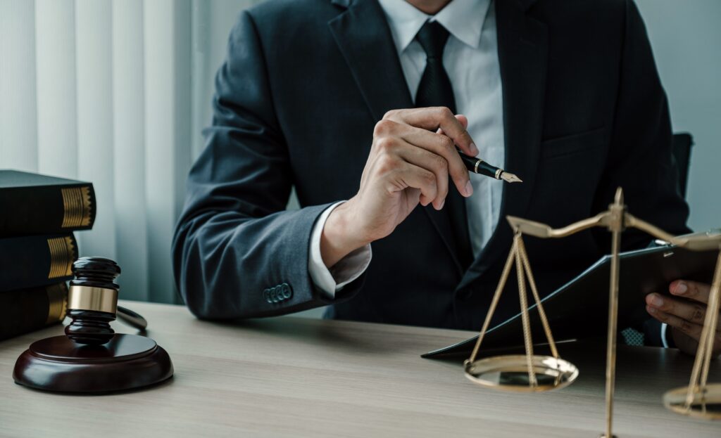 Lawyer hand holding pen and providing legal consult business dispute service to the man at the office with justice scale and gavel hammer.