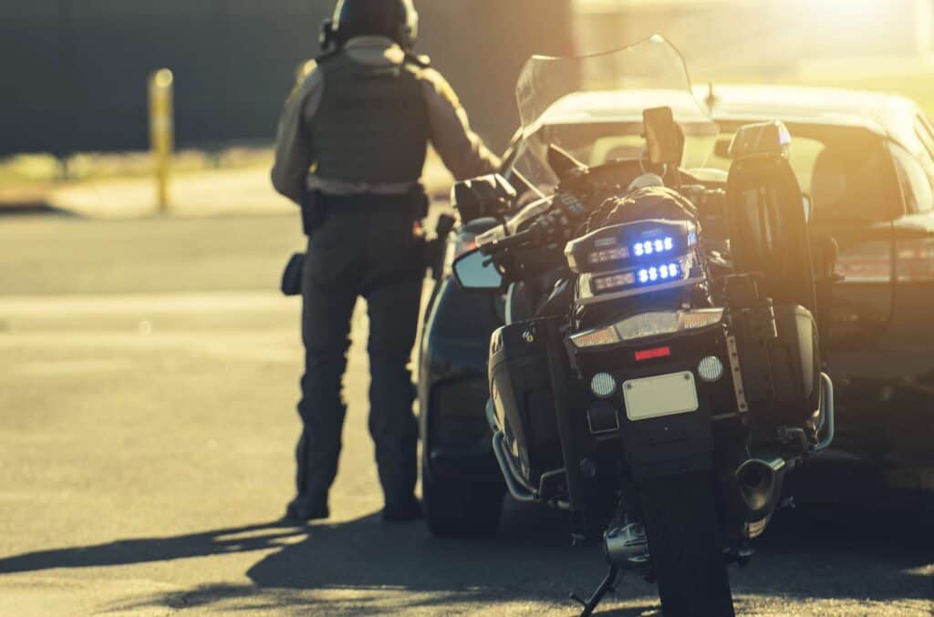 Police officer with motorcycle and car during traffic stop at sunset.
