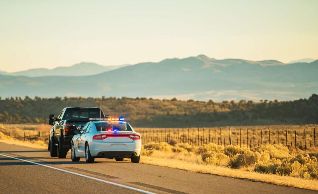Police car with flashing lights on a rural highway in Arizona, with mountains in the background.